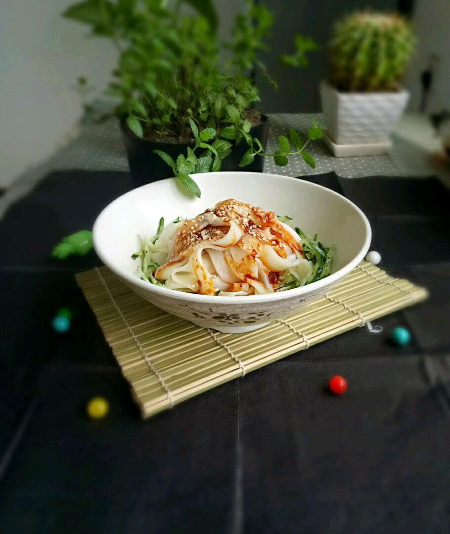 把黄瓜丝和切好的凉皮,放入碗中,撒上蒜末,淋上料汁,再撒上白芝麻