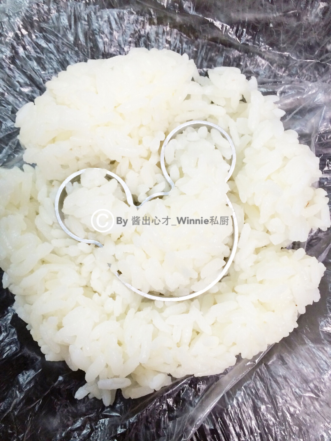8. 然后取模具在凉开水中浸泡一下后平压在饭饼中间,不平整的地方用保鲜袋覆盖着再按压平整,务必要结实,然后戴上一次性手套。慢慢从模具中推出米饭团即可摆盘。另外制作了加入黑芝麻的米奇饭团,这样看着更丰富一些。(忘记把成品饭团拍照了,请原谅喔)