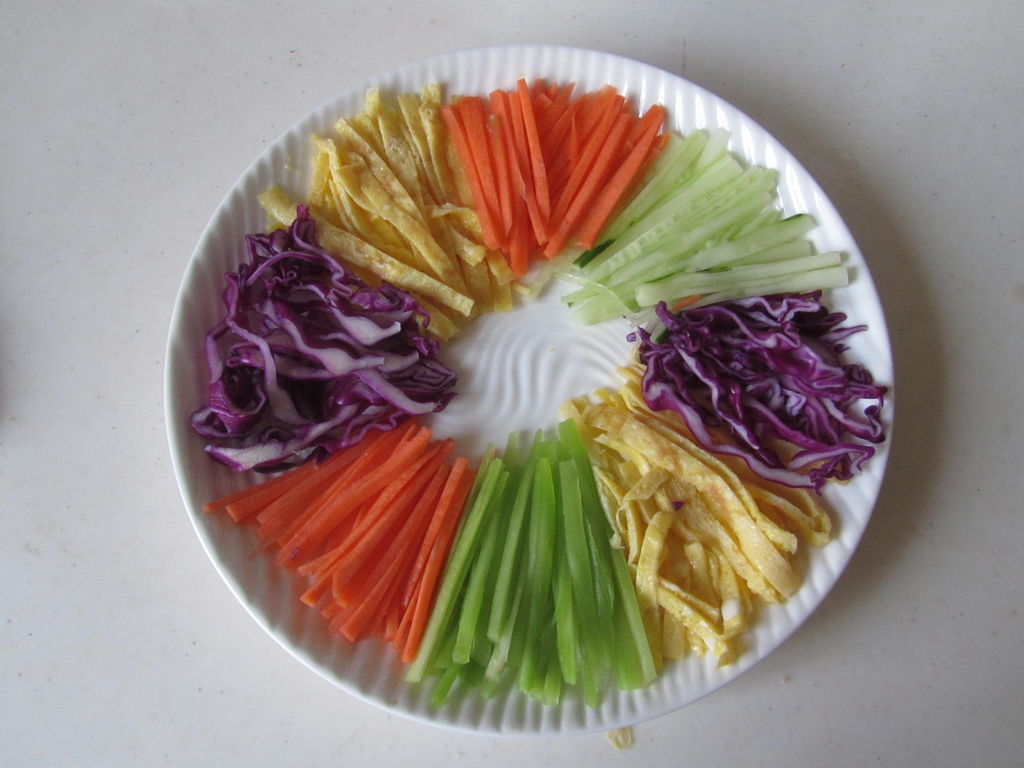 将准备好的五彩蔬菜丝围边平铺在盘子中